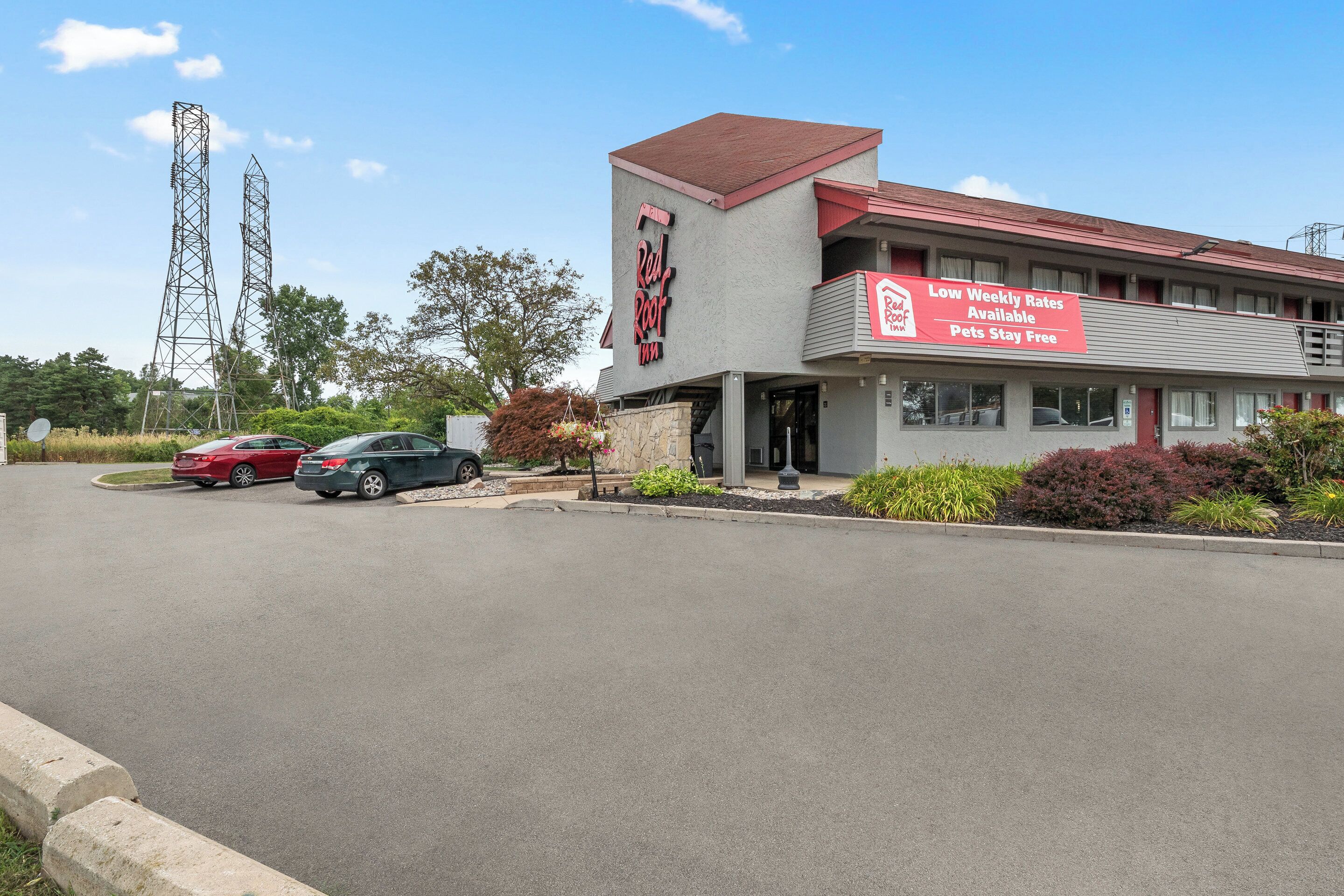 A Red Roof Inn with a sign advertising low weekly rates and a parking lot with several cars.