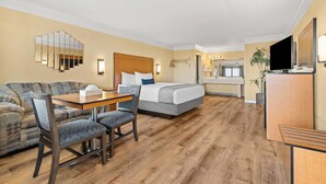 Una habitación de hotel con cama, sofá, mesa de comedor con sillas, televisor y espejo.