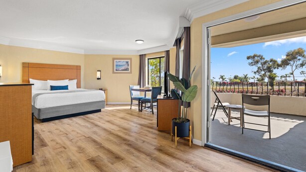 Habitación de hotel con cama, escritorio, silla y balcón con vistas.