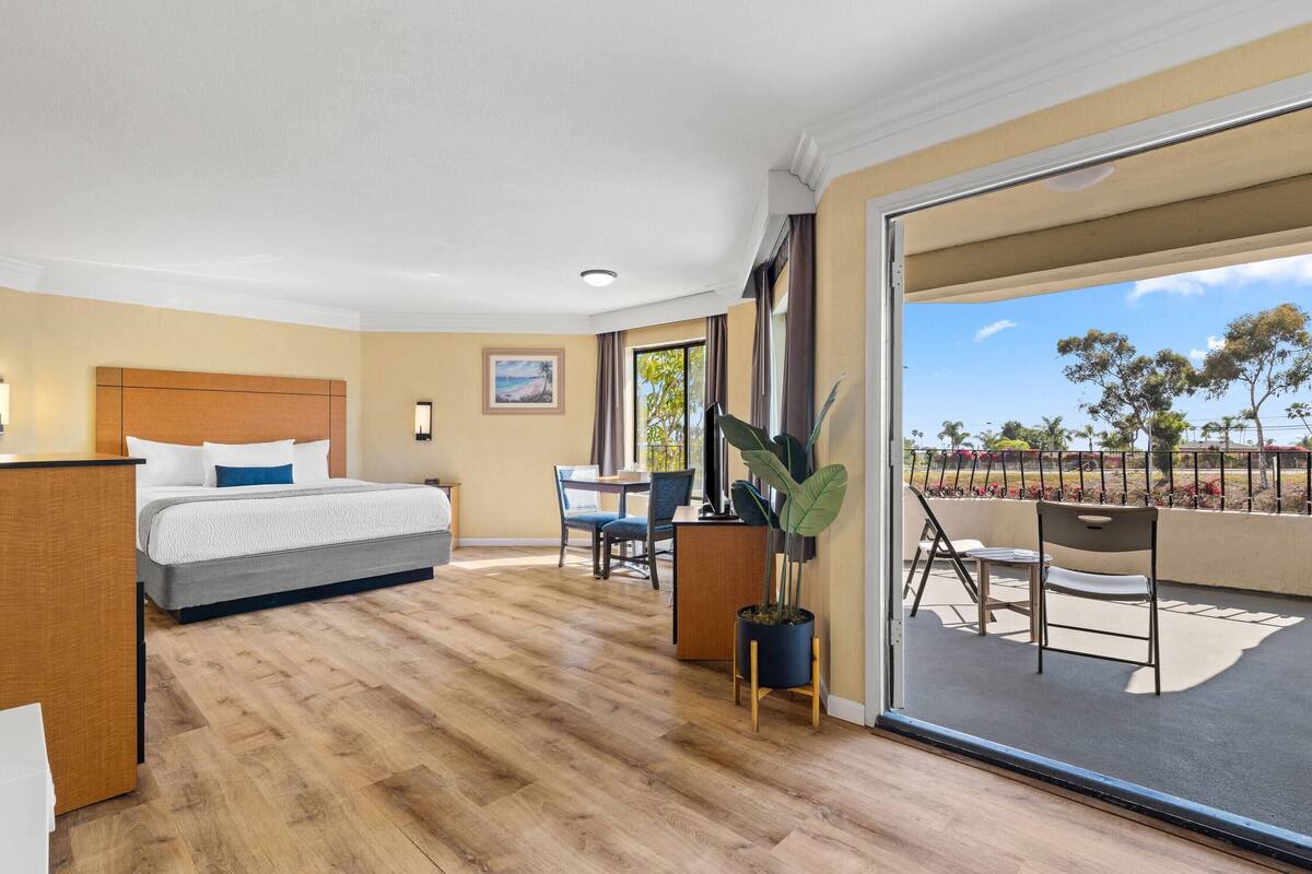 A hotel room with a bed, a desk, a chair, and a balcony with a view.