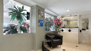 Zona de recepción con una mesa de vidrio, una butaca de cuero negro, una planta grande en maceta y un televisor montado en la pared.