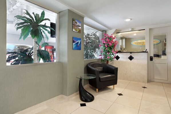 A reception area with a glass-top table, a black leather chair, a large potted plant, and a wall-mounted TV. - Travelodge by Wyndham San Clemente Beach (San Clemente)