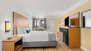 A hotel room with a bed, bedside table, TV, and a small kitchenette.