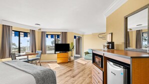 Una habitación de hotel con una cama, un escritorio con una silla, un televisor, una cafetera y un refrigerador.