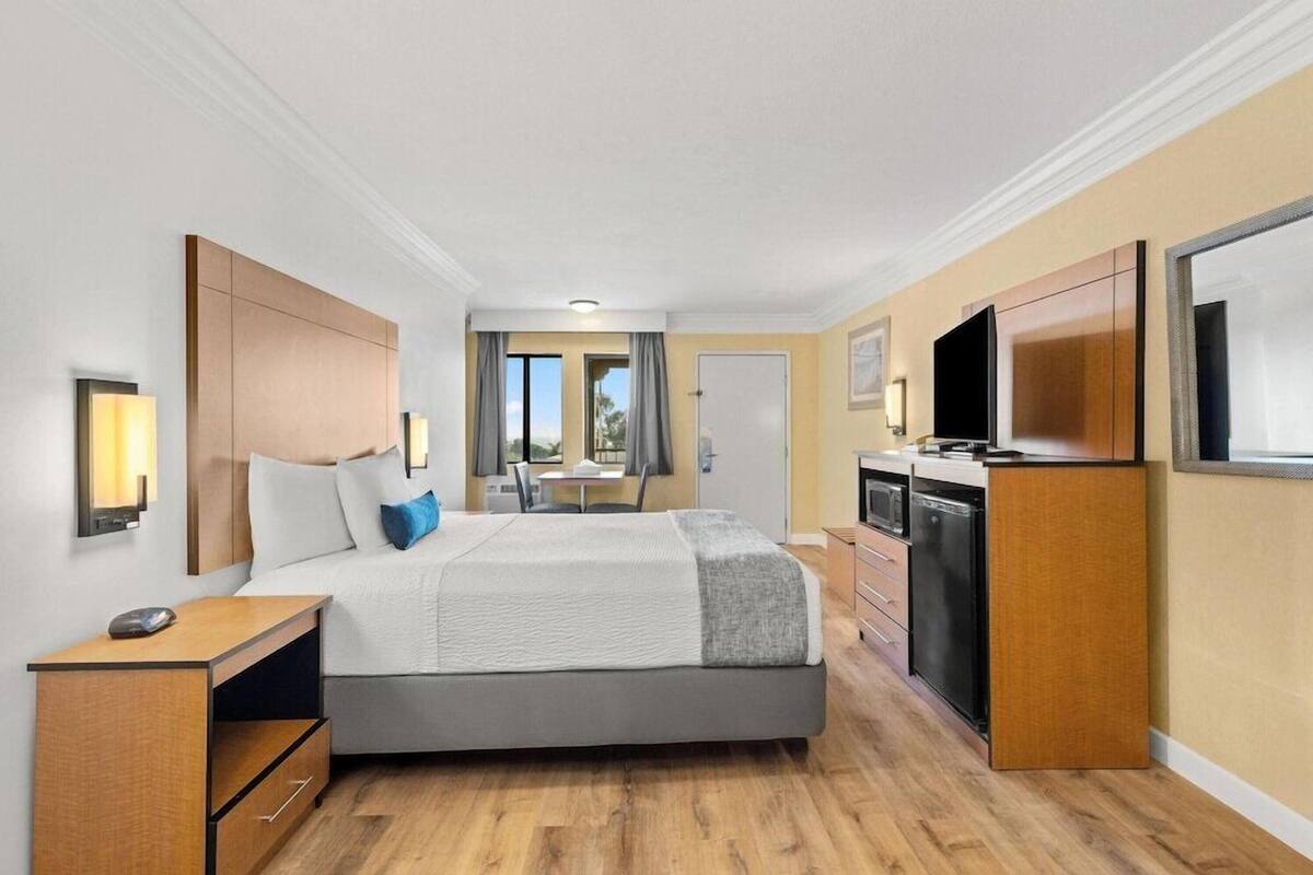 A hotel room with a bed, bedside table, TV, and a kitchenette.