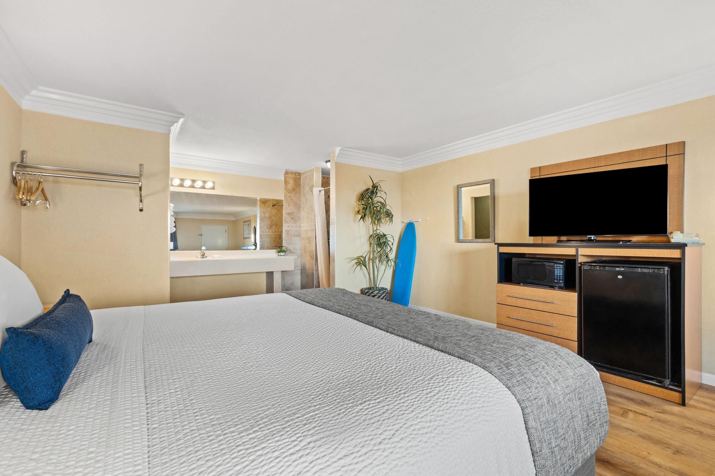 A hotel room with a large bed, a television, a microwave, and a refrigerator.