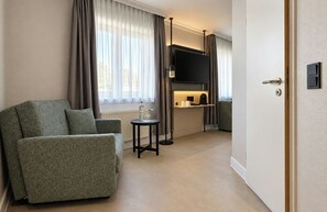 A hotel room with a sofa, a small table, a television, and a minibar.