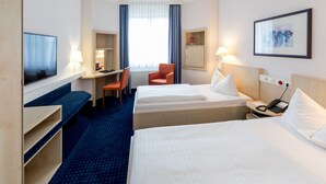 A hotel room with two beds, a desk, a chair, a television, a lamp, and a framed picture on the wall. - Hotel Magdeburg City Center by Leonardo Hotels (Magdeburg)