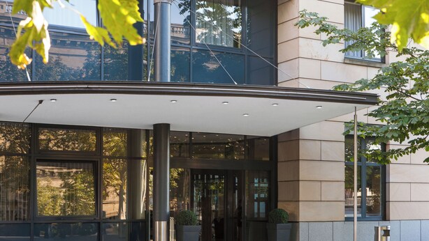 A modern building entrance with large glass windows, a covered entryway, and potted plants. - Hotel Magdeburg City Center by Leonardo Hotels (Magdeburg)