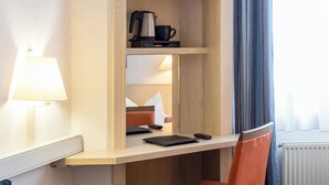 A hotel room with a desk, a lamp, a chair, a bed, and a window with curtains. - Hotel Magdeburg City Center by Leonardo Hotels (Magdeburg)