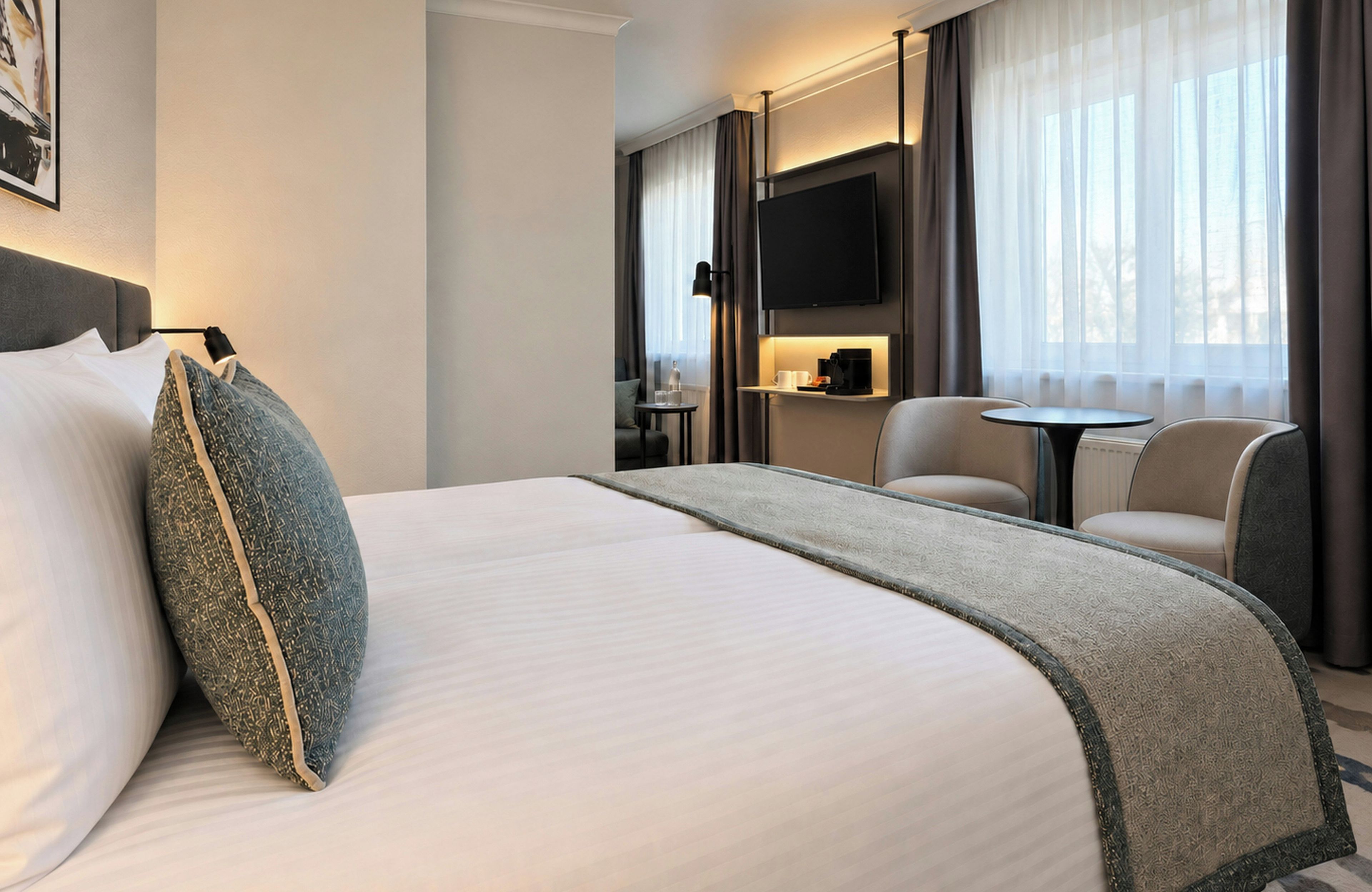 A hotel room with a large bed, a flat-screen TV, a coffee machine, and a seating area with two chairs.