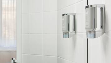 Ein modernes Badezimmer mit weißen Fliesen und zwei verchromten Seifenspendern an der Wand.