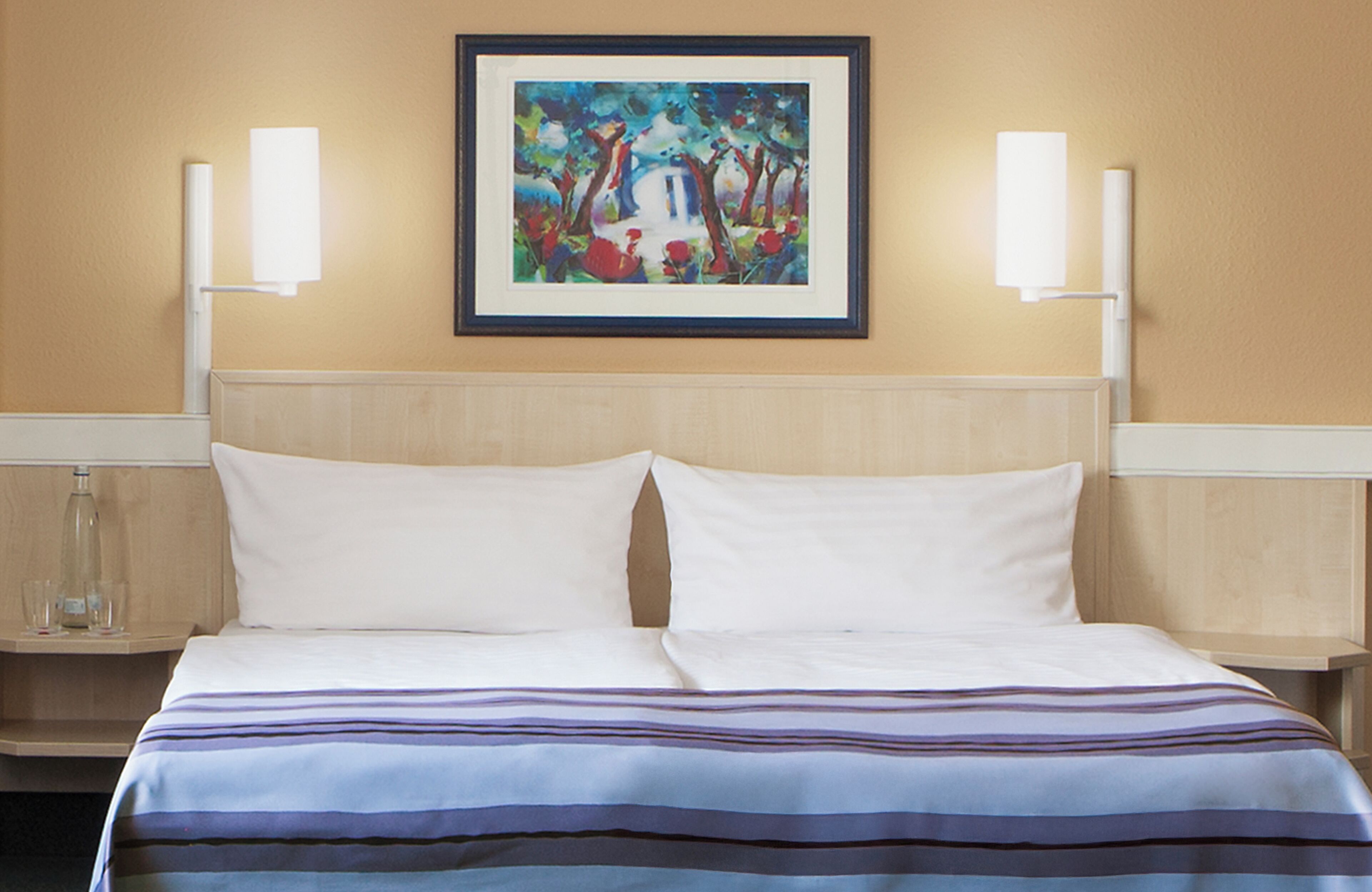 Ein Hotelzimmer mit einem Bett, zwei Nachttischen, einem gerahmten Gemälde an der Wand und zwei Wandlampen.