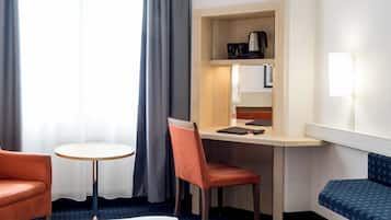 A hotel room with a bed, a desk with a chair, a small round table, a sofa, and a bench.