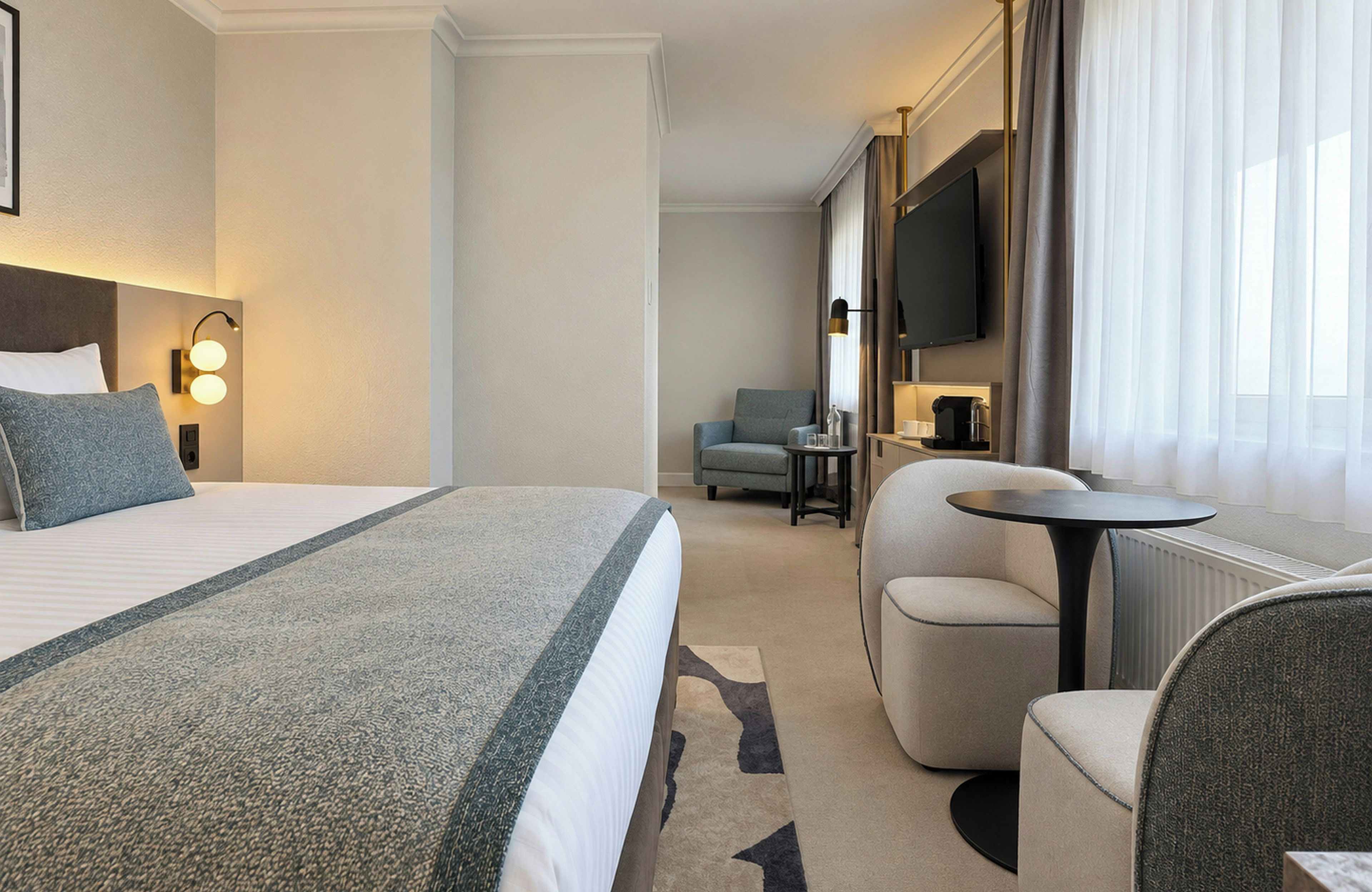 Habitación de hotel con cama, escritorio, silla, televisión y ventana con cortinas.