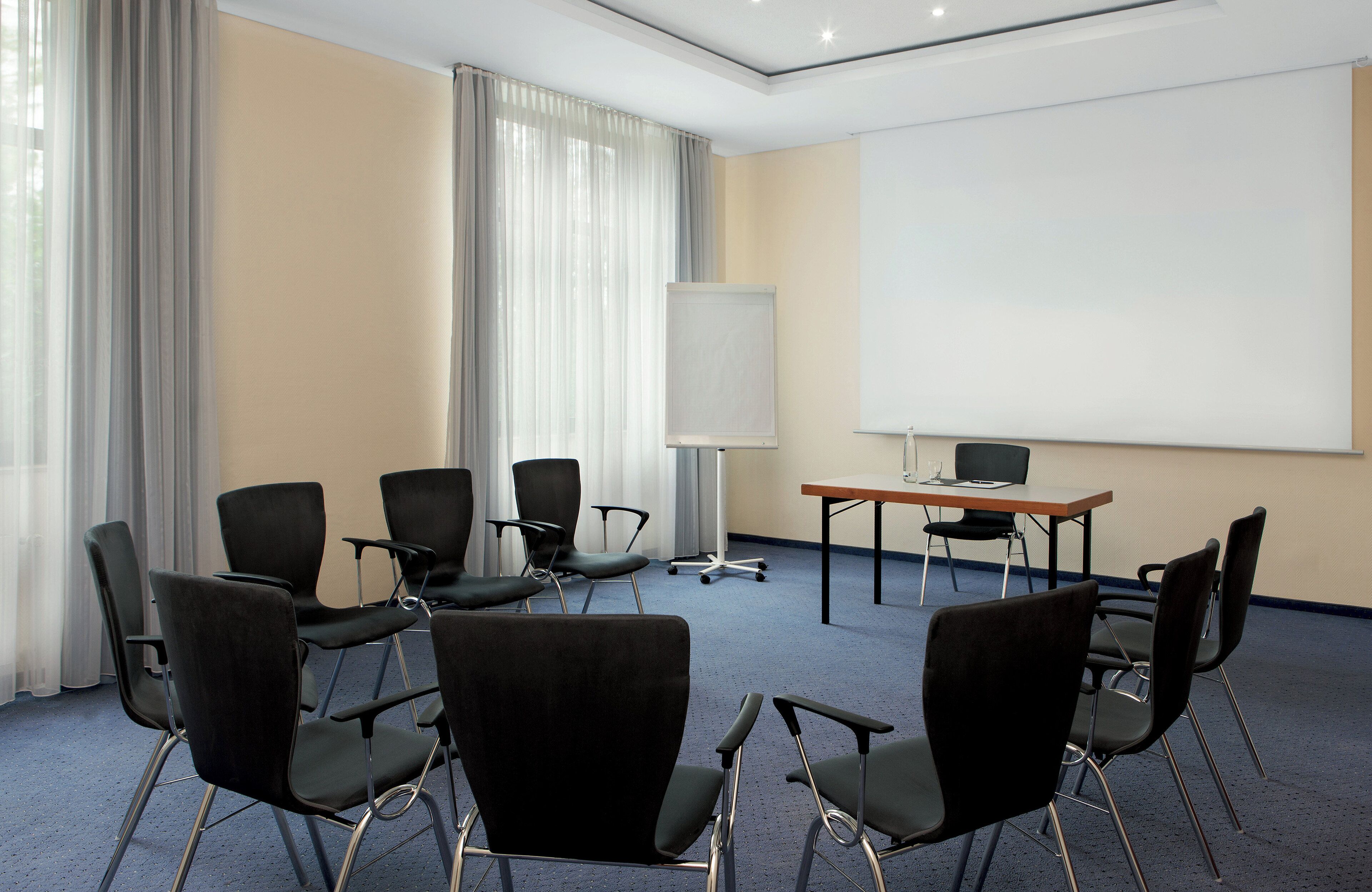 Un salón de conferencias con una pantalla grande, una mesa de madera y sillas negras dispuestas alrededor.