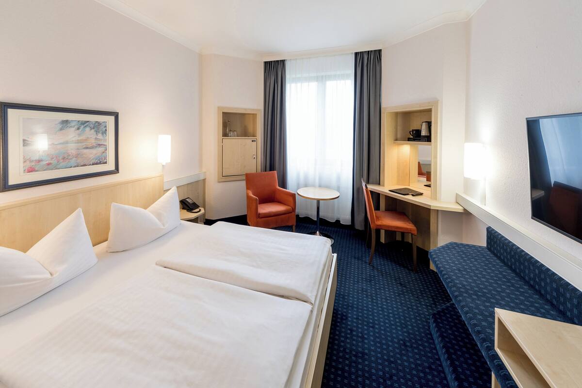 Ein Hotelzimmer mit einem großen Bett, einem Schreibtisch mit Stuhl, einem Fernseher und einem Bild an der Wand.