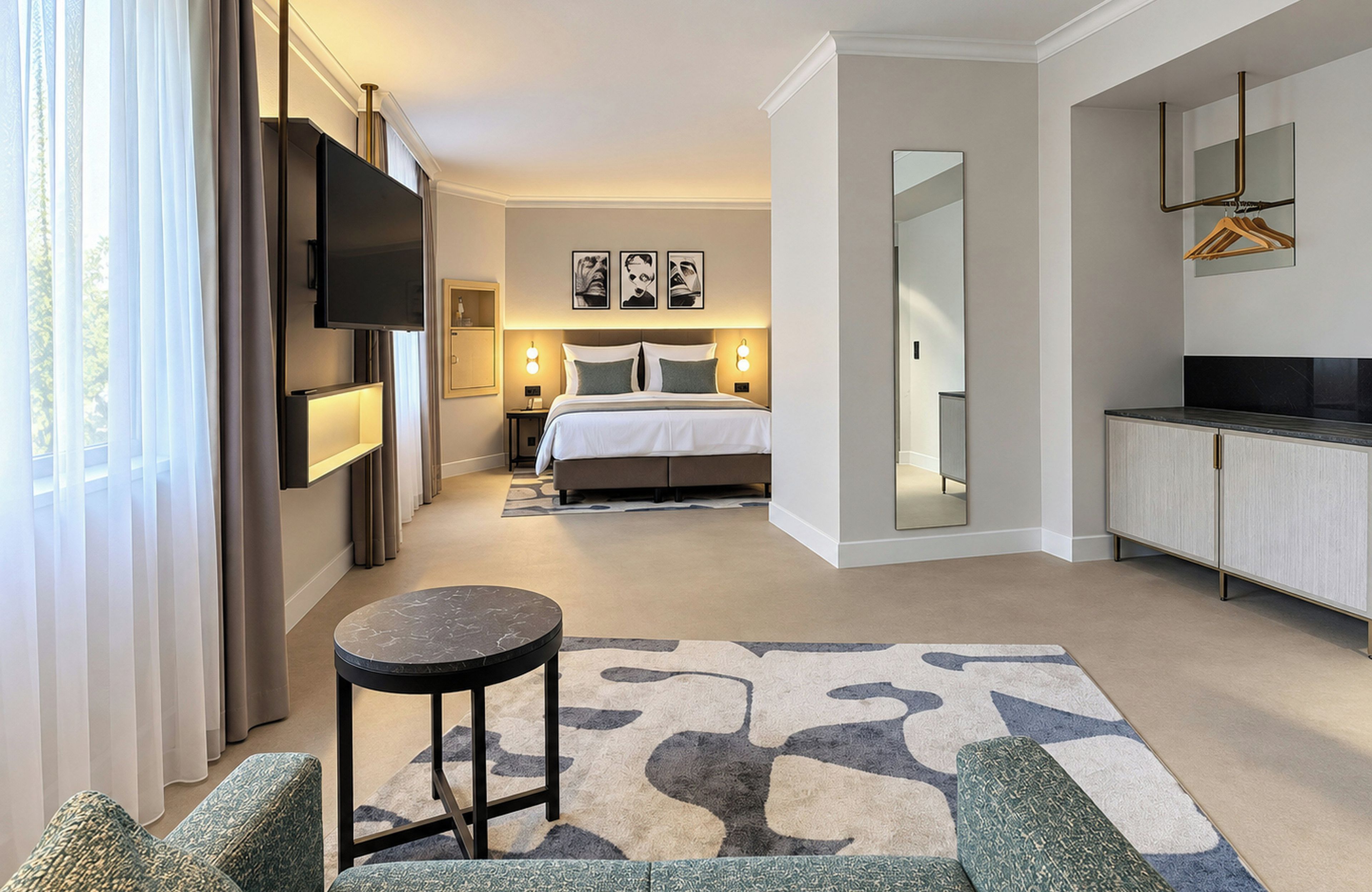 Ein Hotelzimmer mit Bett, Fernseher, einer Sitzecke mit Tisch und einer Küchenzeile.