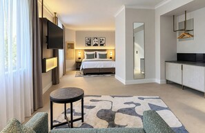A hotel room with a bed, a TV, a seating area with a table, and a kitchenette.