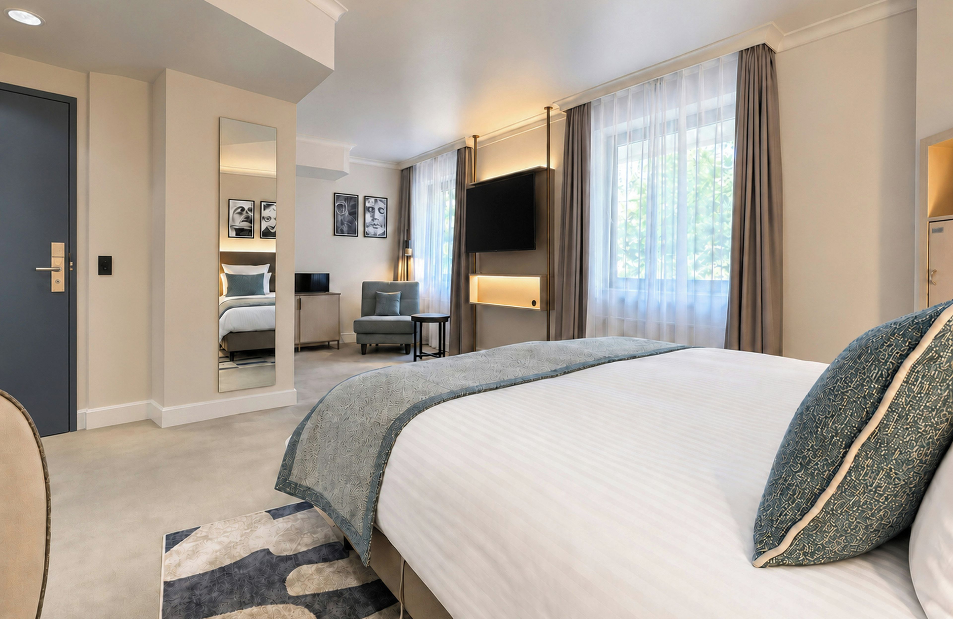 Una camera d'albergo con un letto grande, una scrivania, una sedia, una TV e un bagno visibile attraverso una porta aperta.