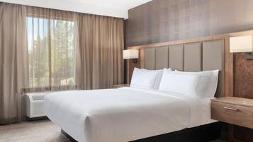 A hotel room with a large bed, a nightstand, a wall-mounted lamp, and a window with curtains.