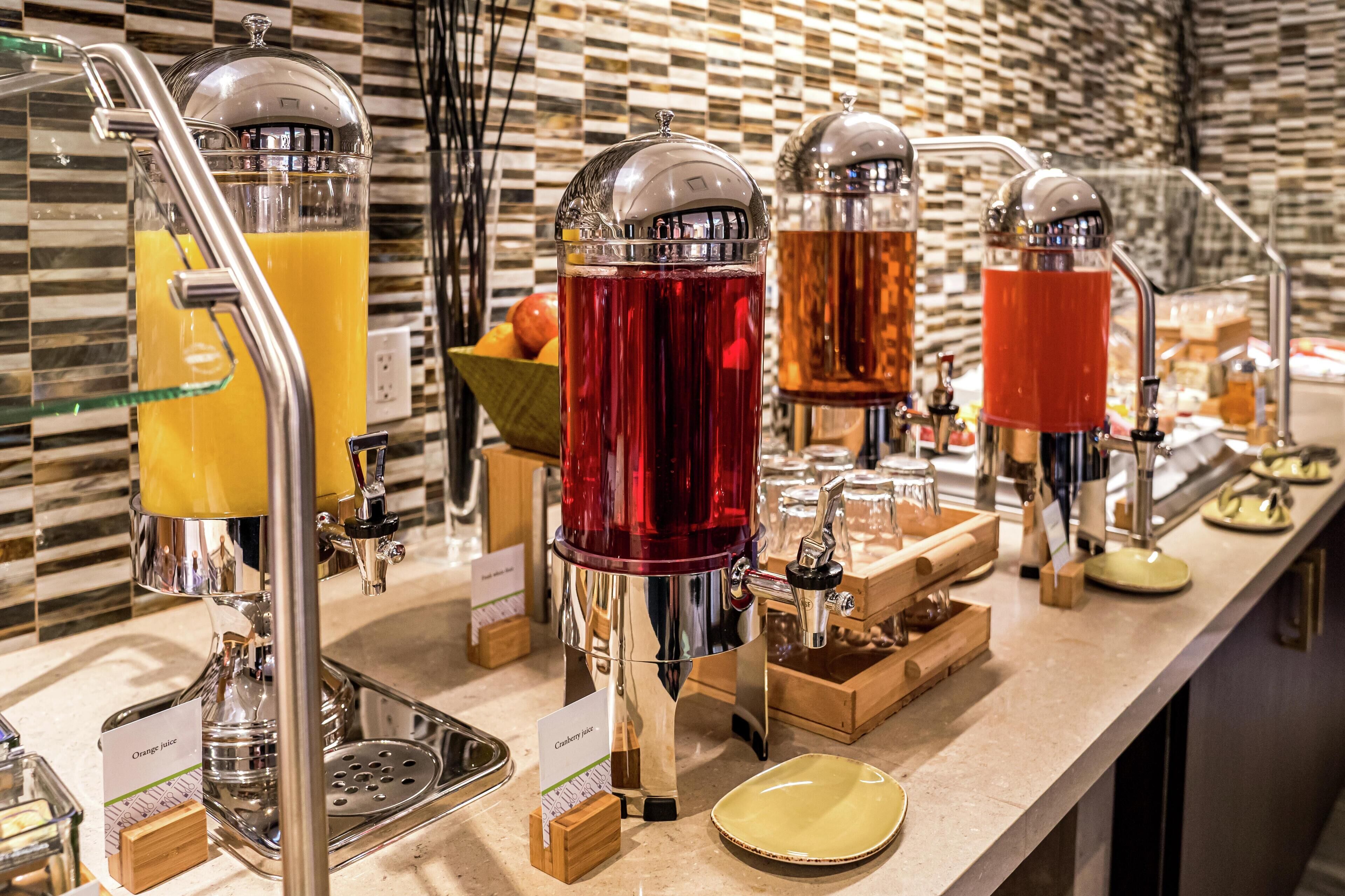 A buffet area with self-serve beverage dispensers for orange juice and cranberry juice.