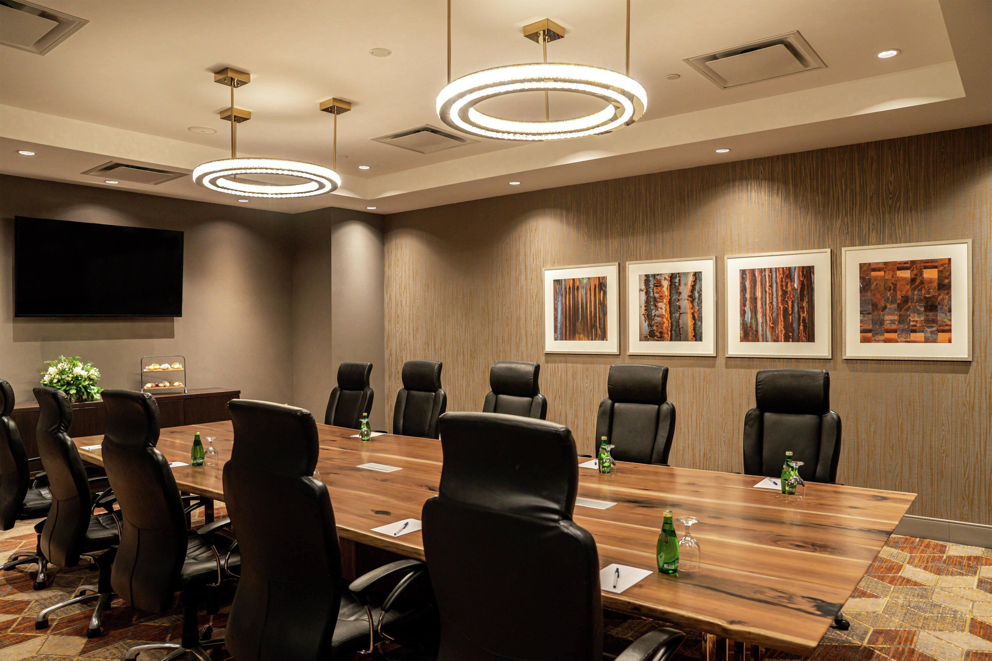 A conference room with a long table, black chairs, a flat-screen TV, and framed artwork on the wall.
