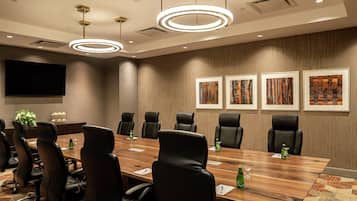 A conference room with a long table, black chairs, a flat-screen TV, and framed artwork on the wall.