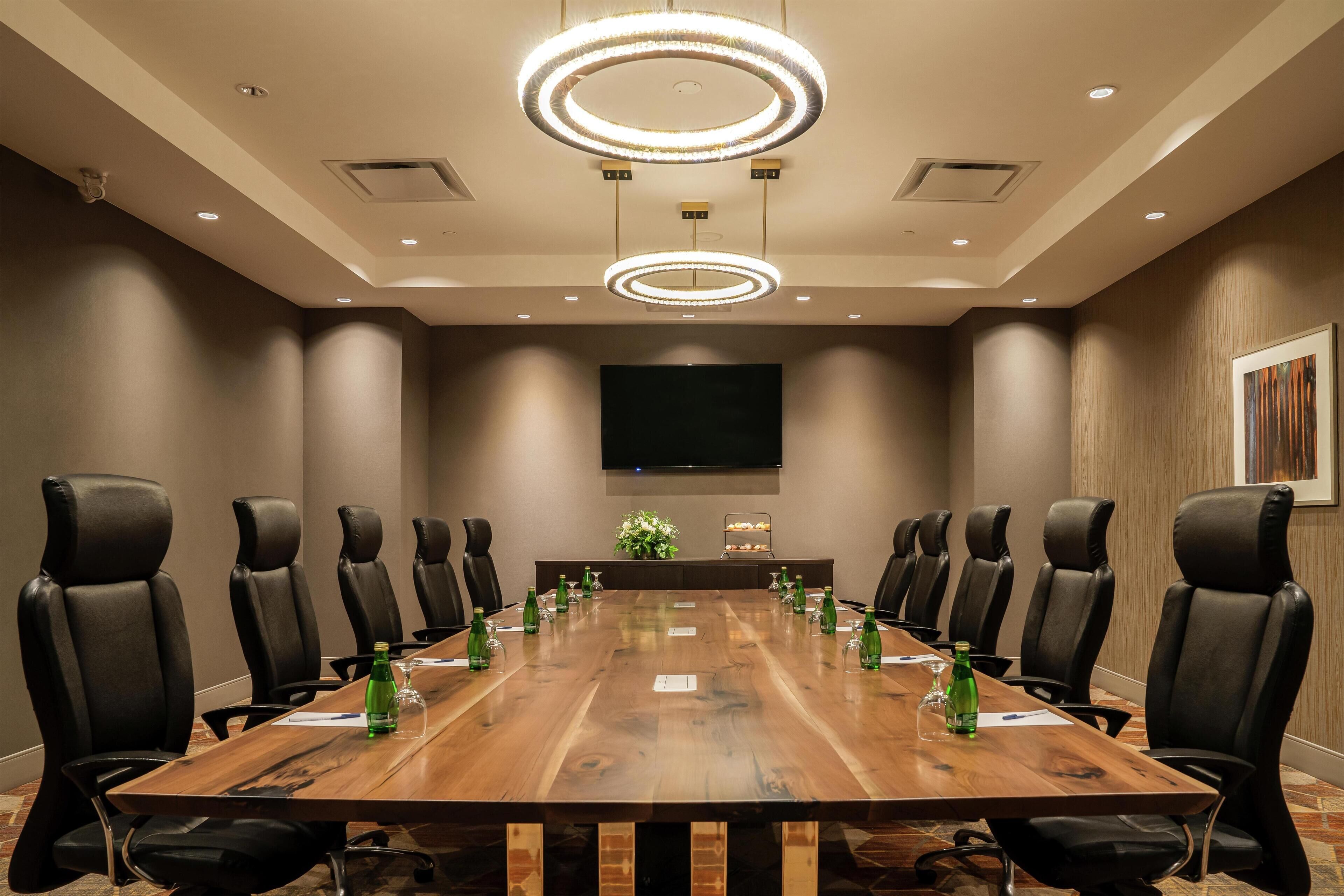 Un salón de conferencias con una larga mesa de madera, sillas de cuero negro y un televisor de pantalla plana grande en la pared.