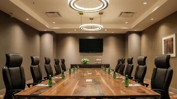 Un salón de conferencias con una larga mesa de madera, sillas de cuero negro y un televisor de pantalla plana grande en la pared.