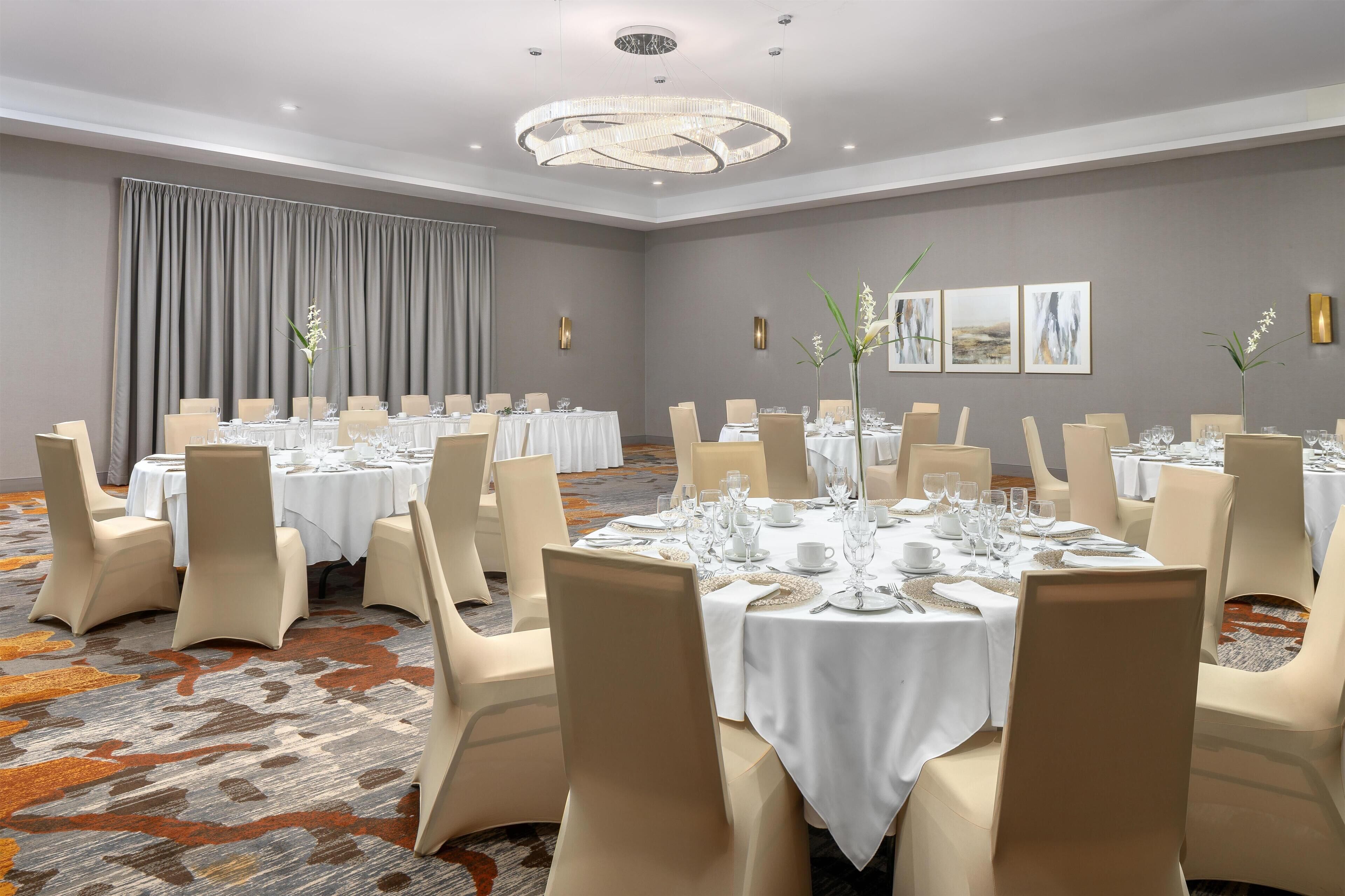 A conference room with multiple round tables, each set with white tablecloths, chairs, and glassware.