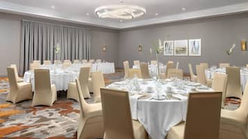 A conference room with multiple round tables, each set with white tablecloths, chairs, and glassware.