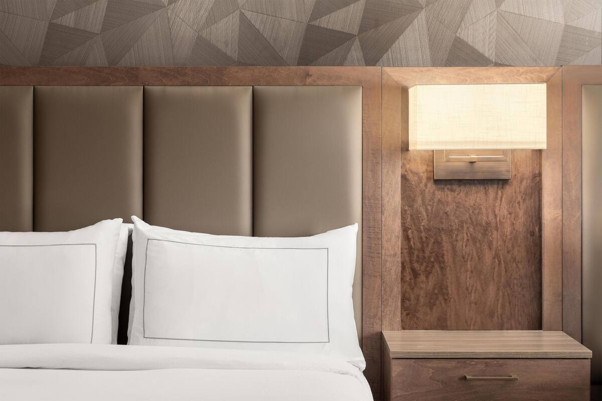 A hotel room with a large bed, a nightstand, and a wall-mounted lamp.