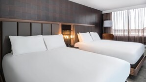 A hotel room with two beds, a large window with curtains, and a modern headboard design.