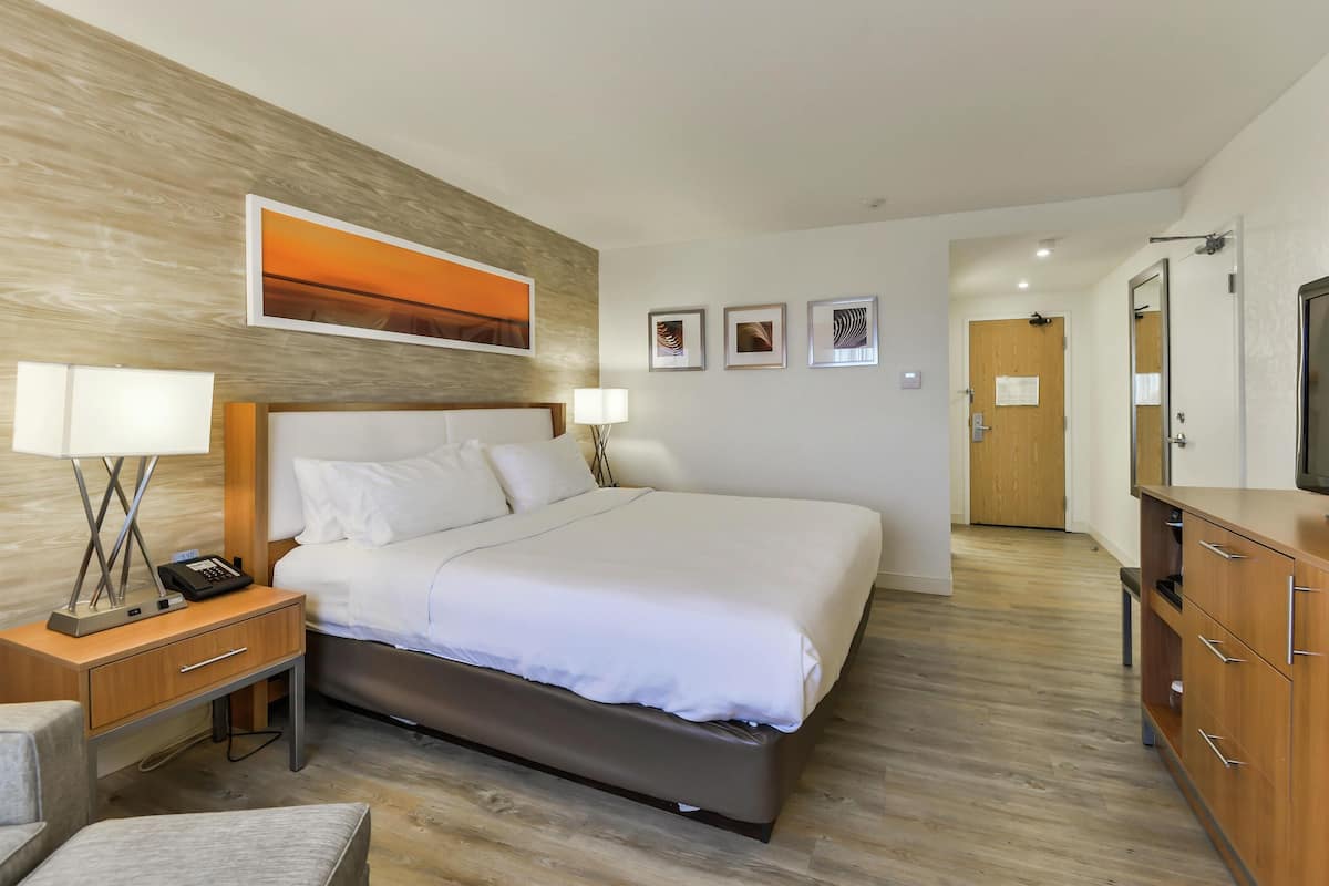 A modern hotel room with a large bed, bedside tables, a desk, and a wardrobe.