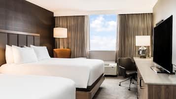 Ein Hotelzimmer mit zwei Betten, einem Schreibtisch, einem Fernseher und einem Fenster mit Vorhängen.