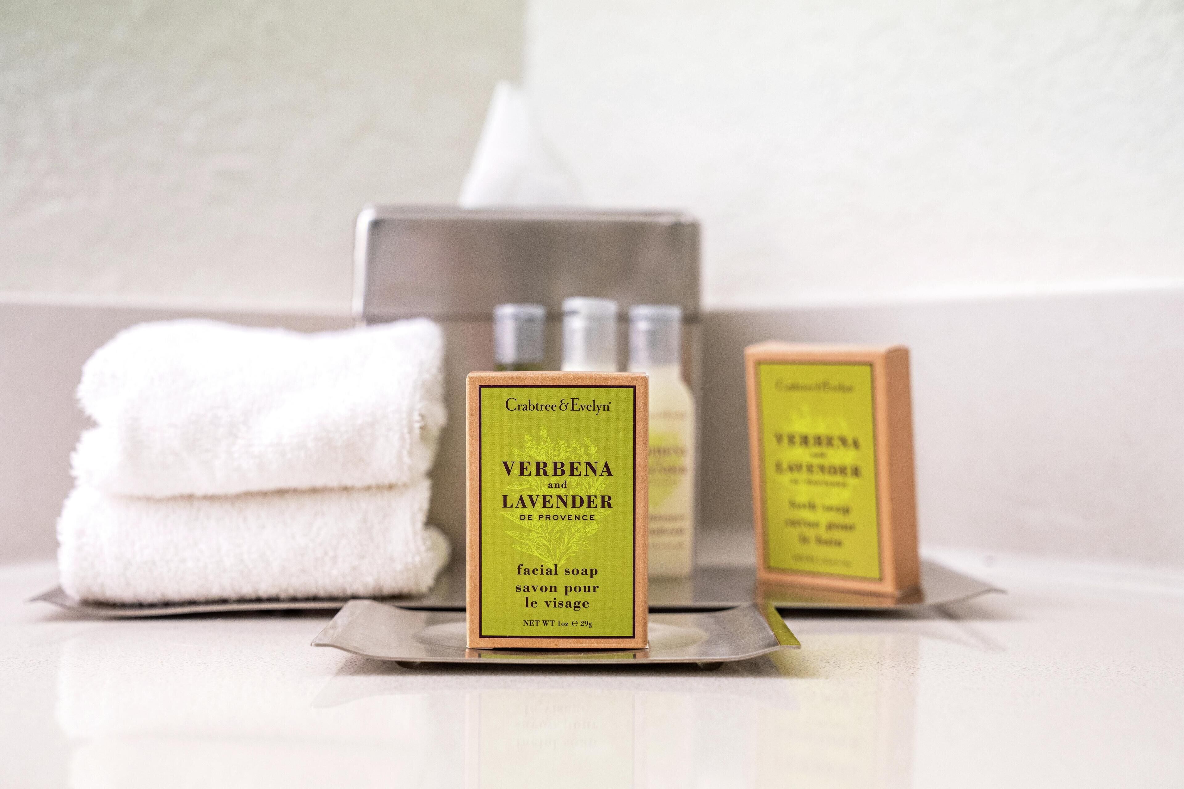A bathroom with a stack of white towels, a box of facial soap labeled 'VERBENA and LAVENDER', and a tissue box.