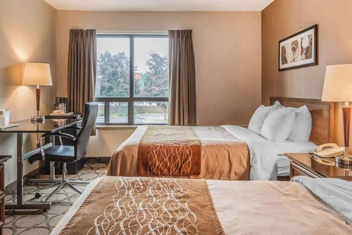 Une chambre d’hôtel équipée d’un lit, d’un bureau, d’une chaise, de lampes et d’une fenêtre avec des rideaux.