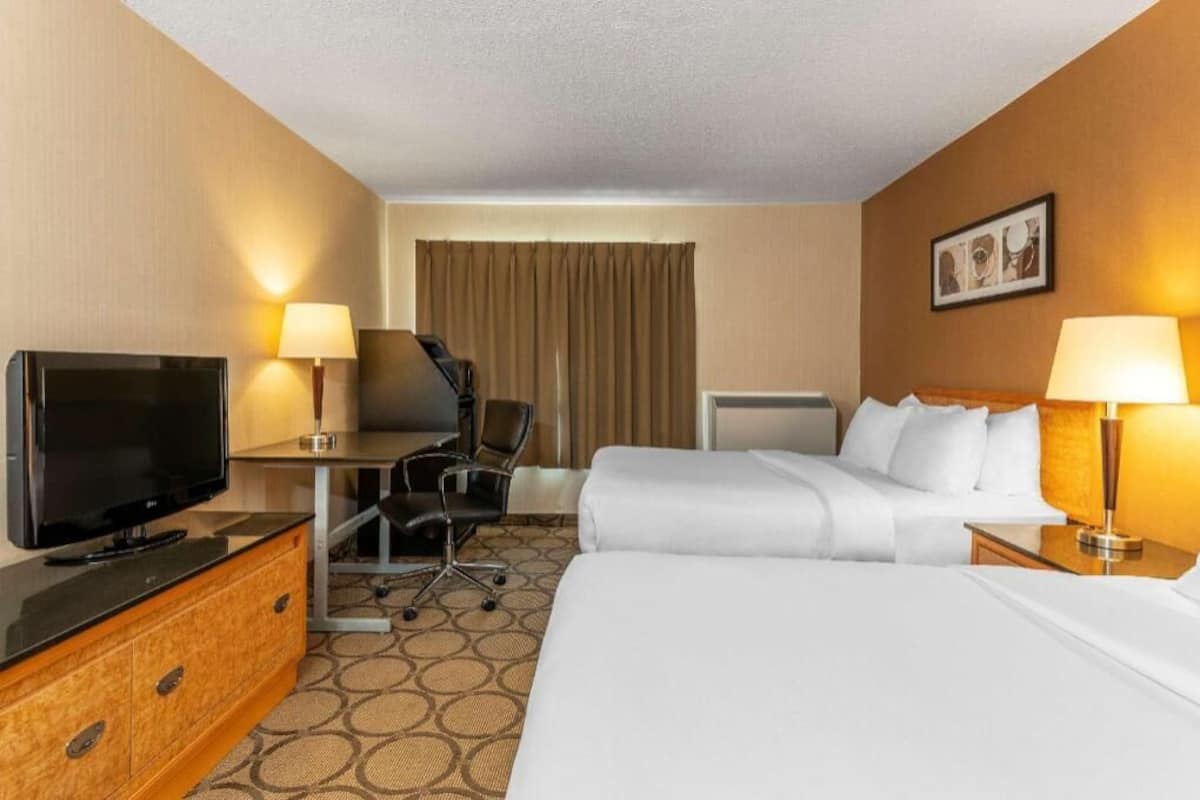 Une chambre d’hôtel avec un lit, un bureau avec une télévision, une chaise, une lampe et un tableau au mur.