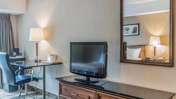 Quarto de hotel com televisão de tela plana, escrivaninha de madeira, cadeira, cômoda e um espelho grande.