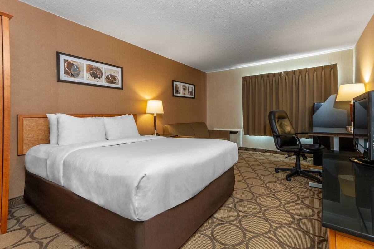 Une chambre d’hôtel avec un grand lit, un bureau avec une chaise, une télévision et deux lampes fixées au mur.