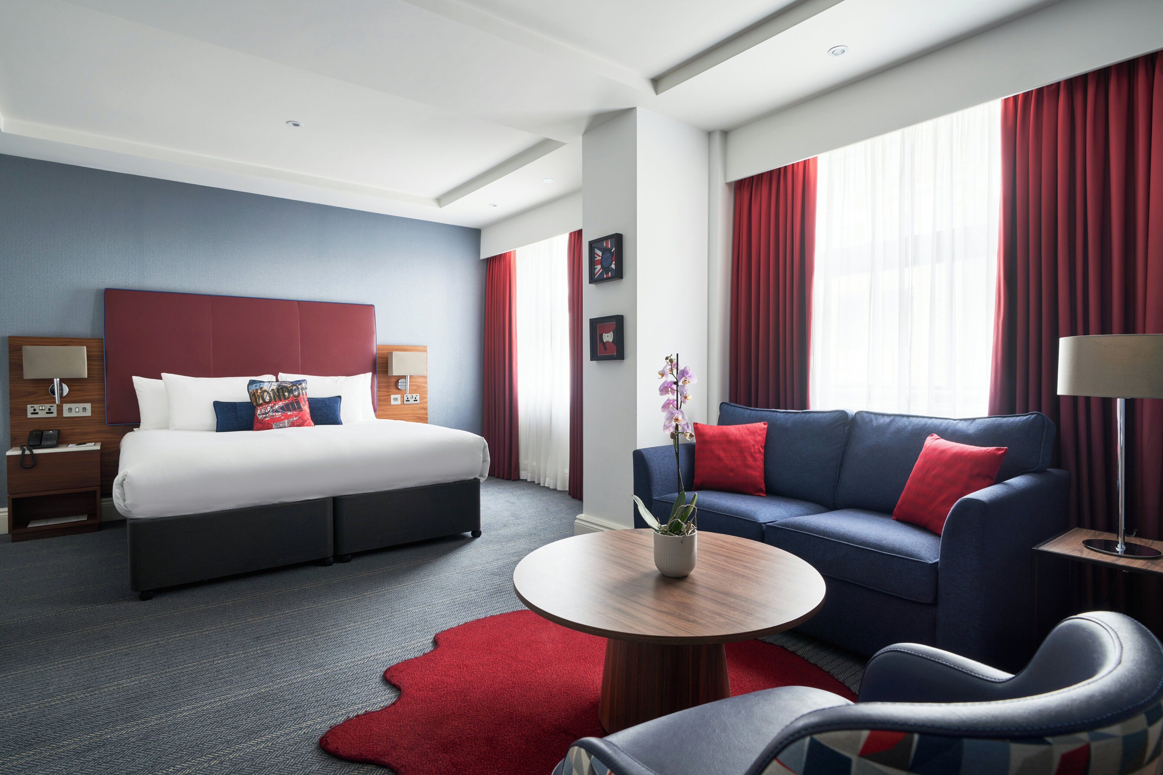 A hotel room with a bed, a sofa, a coffee table, and a red rug.