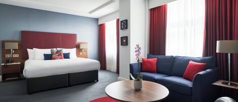 Una habitación de hotel con cama, sofá, mesa de centro y alfombra roja.