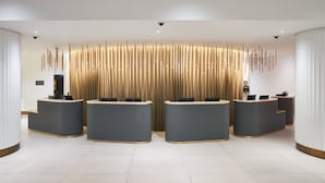 A reception area with four curved reception desks, a modern light fixture, and a security camera on the ceiling. - The Cumberland, London (London)