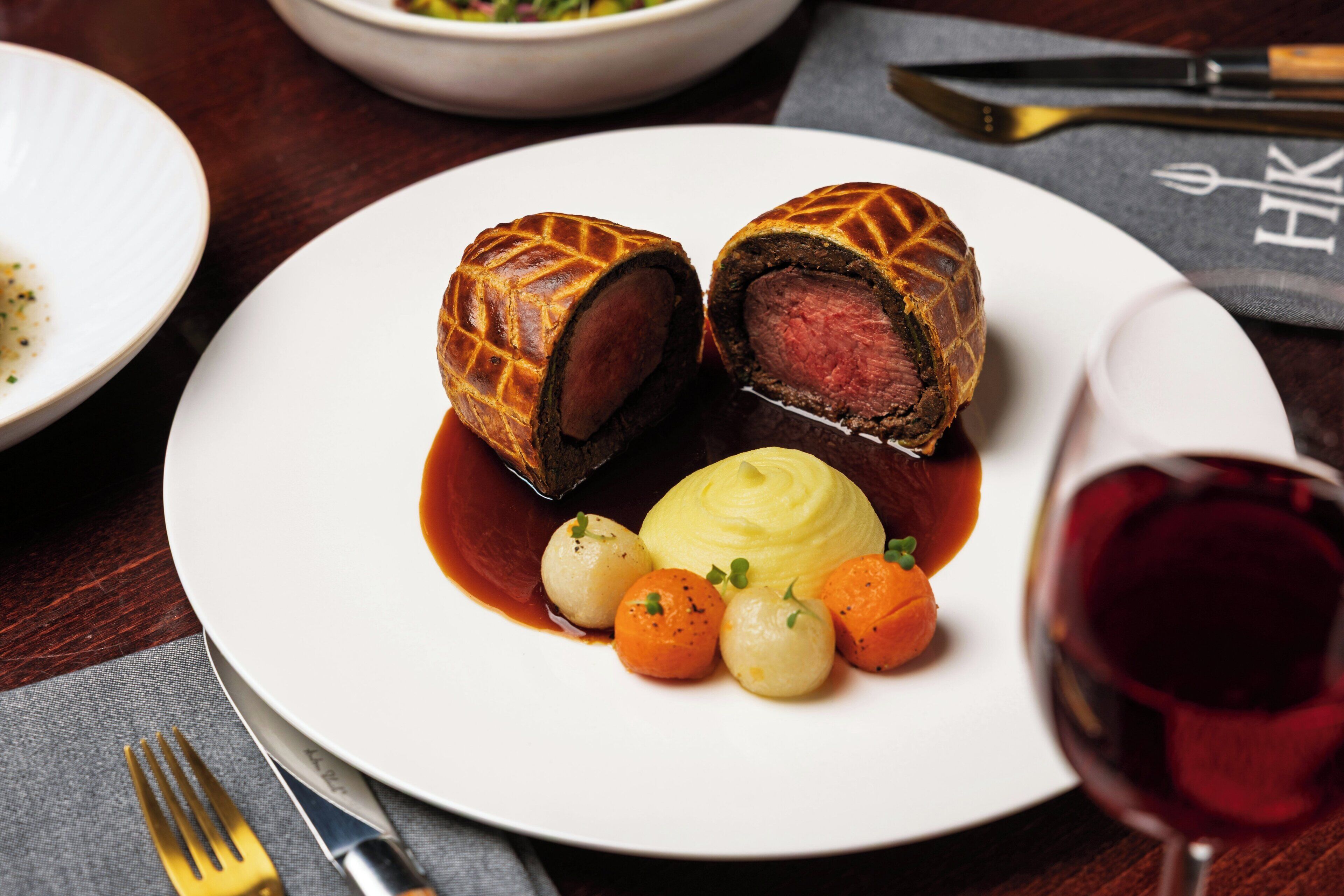 Un plato con un wellington de ternera, puré de patatas y verduras pequeñas.
