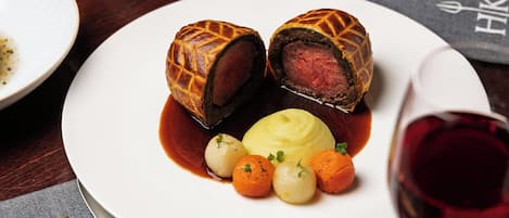 Un plato con un wellington de ternera, puré de patatas y verduras pequeñas.