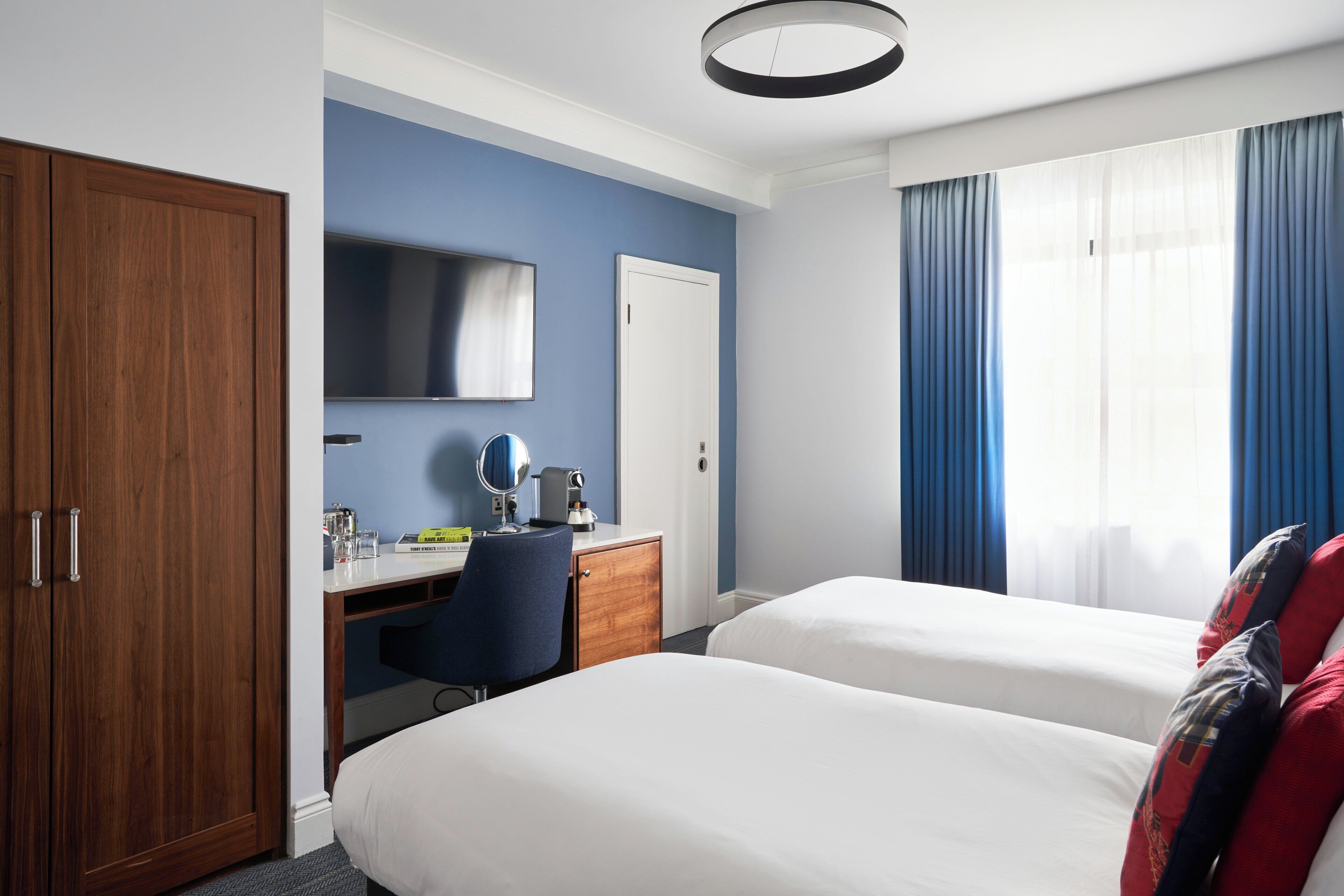 Une chambre d’hôtel avec deux lits, un bureau, une armoire, une télévision et une fenêtre avec des rideaux.