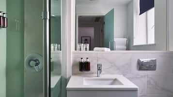 Un baño moderno con ducha envuelta en vidrio, un lavabo blanco sobre encimera de mármol y un inodoro.