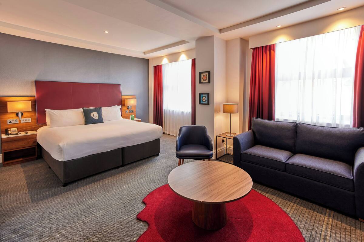 Ein Hotelzimmer mit Bett, Sofa, rundem Tisch, Nachttisch und Lampe.
