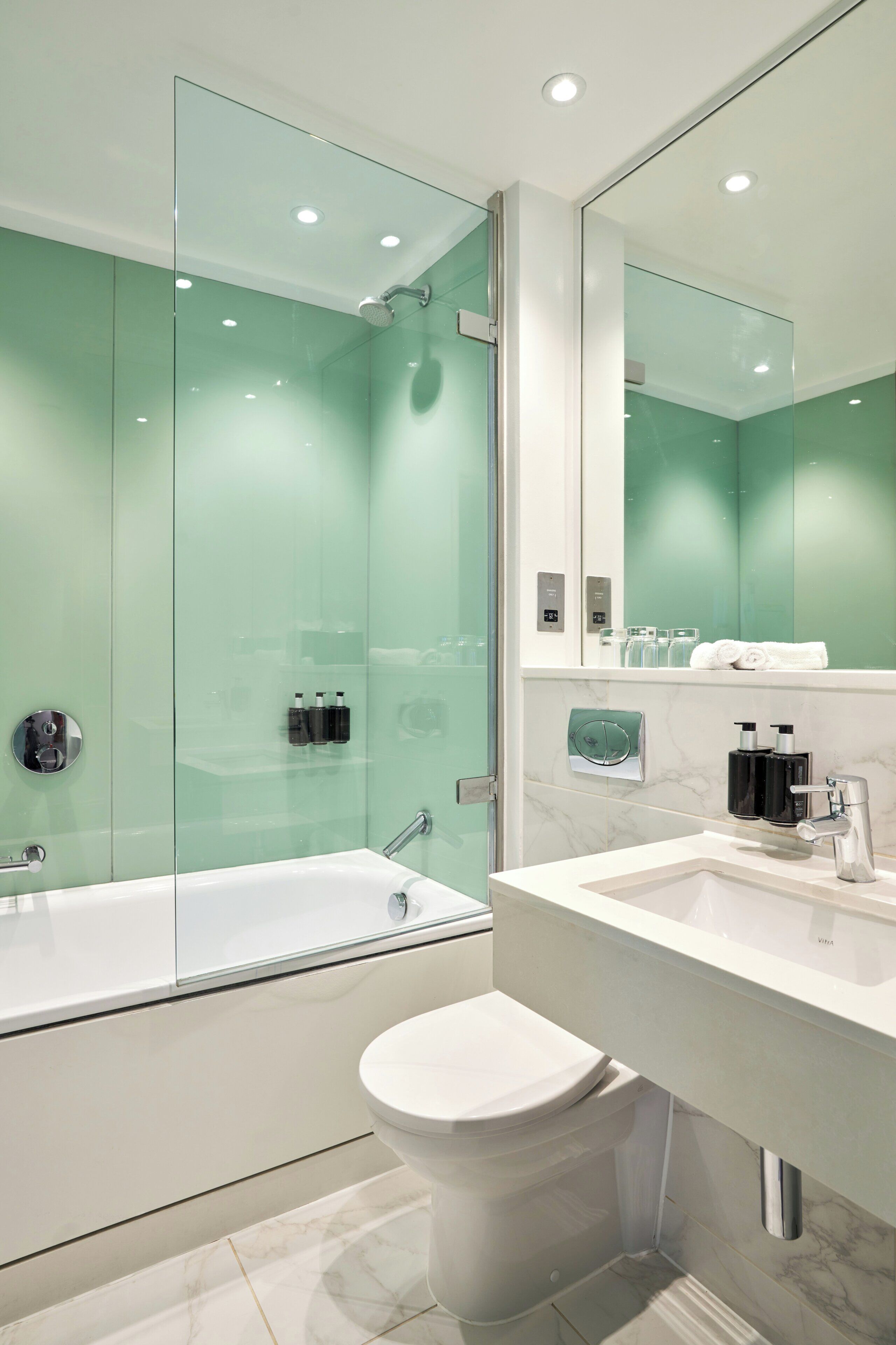 Ein modernes Badezimmer mit einer gläsernen Duschkabine, einer weißen Toilette und einem Boden mit Marmorfliesen.